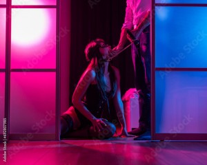 A woman is kneeling in front of a man. BDSM sex concept. Vertical photo. 