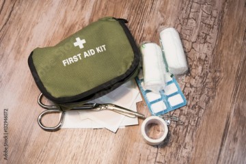 Green first aid kit on wooden background. Bandages, scissors and medicines