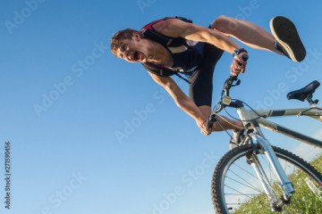 Young man screams while falling from the bicycle in the green field