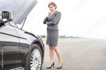 Mature businesswoman looking at breakdown car on road