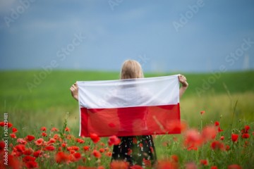 Blond girl holding flag of Poland in the poppy field. Back view. Polish Flag Day. Independence Day. Travel and learn polish language concept.