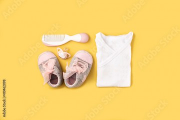 Baby rompers, shoes, pacifier and hair comb on yellow background
