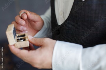Men's hand with two gold wedding rings in the wooden box close up. the groom in black suit holds the wedding rings of white gold on palm on background. wedding ceremony. wedding day. bride and groom