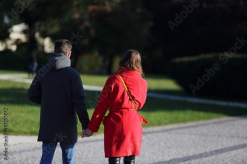  Para młodych ludzie, kobieta i mężczyzna spaceruje deptakiem, chodnikiem w parku. 