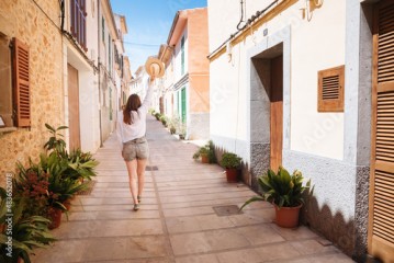 woman walking in the street. Woman holds up her straw hat. Feeling of freedom on vacation. Holiday or vacation in Spain or Greece 