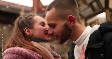 Close-up of the faces of a young couple in love kissing and hugging on the street on a gloomy autumn day.