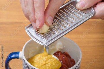 Ścierać ząbek czosnku na tarce, doprawiać sos