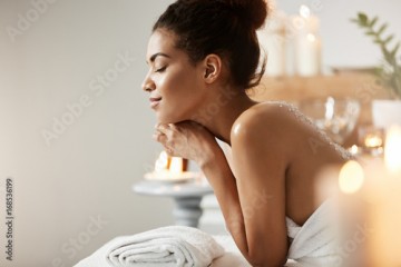 Portrait of pleased african girl relaxing with closed eyes in spa salon.