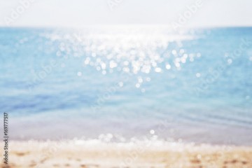 Blurred background sea. Abstract summer background. Glare of the sun against the sea, beautiful bokeh. Yellow sand on the beach and the blue sea.