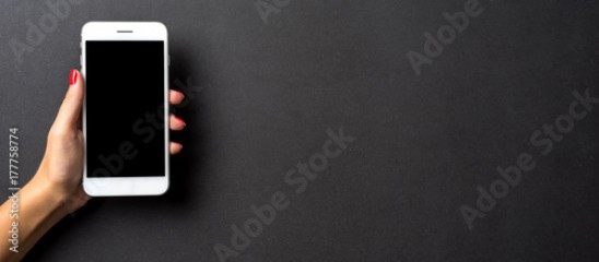 Female hand holding white mobile phone against dark elegant background