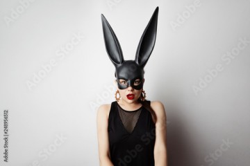 Sexy young woman with red lipstick and large breasts wearing a black mask. Easter bunny standing on a white background and looks very sensually.