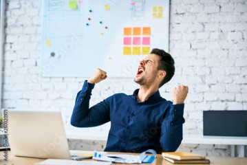 Ecstatic web developer screaming in joy and making gestures celebrating success while sitting in office