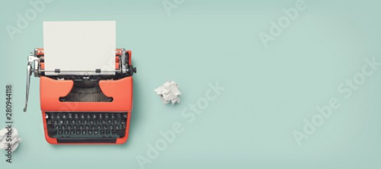 retro banner with red vintage typewriter with a blank sheet of paper and paper balls, top view, copyspace