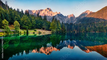 Calm morning view of Fusine lake. Colorful summer sunrise in Julian Alps with Mangart peak on background, Province of Udine, Italy, Europe. Beauty of nature concept background.