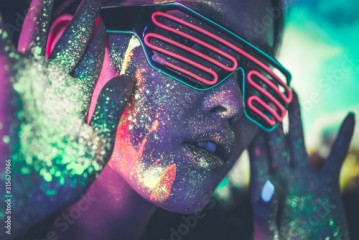 Beautiful young woman dancing and making party with fluorescent painting on her face. Neon facial portraits