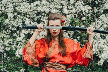 Young girl in traditional kimano in a blooming garden with samurai japanese sword katana in image of warrior woman