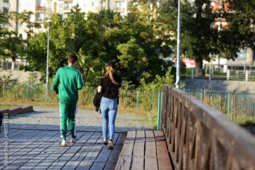 Para młodych ludzie spaceruje deptakiem, chodnikiem w parku, drewniany most, Wrocław. 