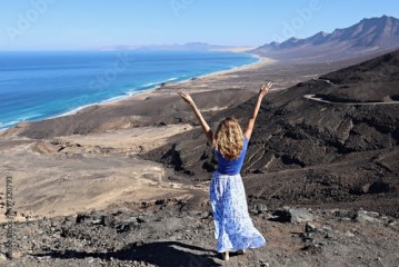 Radosna turystka z rękami do góry stojąca tyłem i podziwiająca piękny widok na plaże Cofete na Fuerteventura