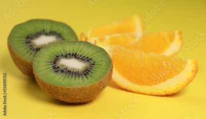 close up of kiwi fruit and orange slices on yellow background 
