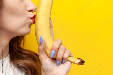 young girl kisses banana and hints at intimacy on yellow background, sexy and erotic concept