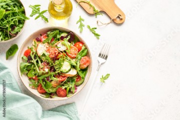 Green salad with baked chicken breast, fresh salad leaves and vegetables. Top view on white background.
