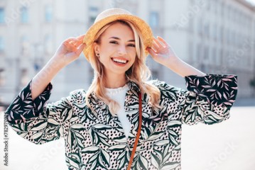 Young beautiful smiling blond hipster woman in trendy summer hippie costume clothes. Carefree female posing in the street. Positive model outdoors at sunset. Cheerful and happy in hat