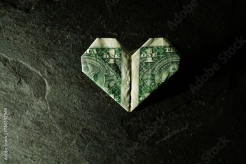 Dollar bill origami heart shape on dark textured background