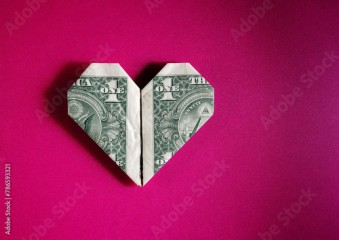 Dollar bill origami heart shape on pink textured background