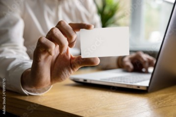 man showing blank business card while working on laptop in office. mockup